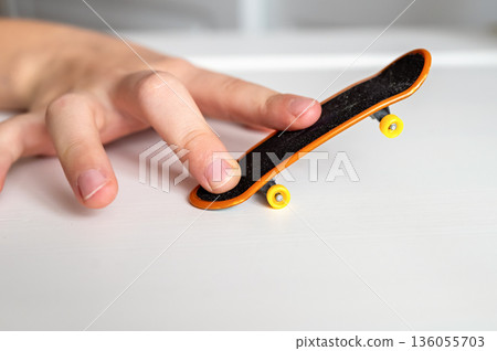 children's hands playing with toy fingerboard with yellow wheels on white background, selective focus 136055703