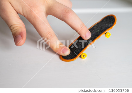 children's hands playing with toy fingerboard with yellow wheels on white background, selective focus 136055706