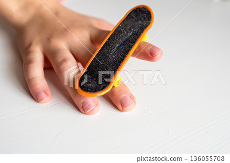 children's hands playing with toy fingerboard with yellow wheels on white background, selective focus 136055708