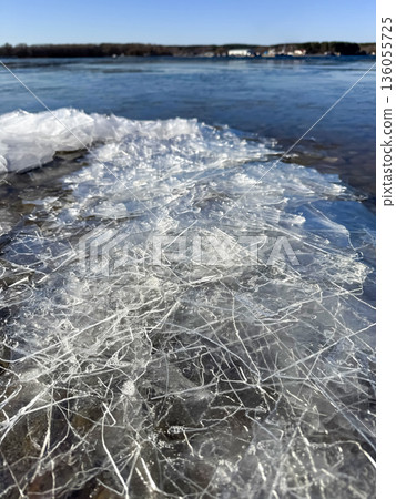 Cracked ice on a rocky shore of a thawed lake under a bright spring blue sky. A contrast of melting cold and warm seasonal renewal Cracked ice on a rocky shore of a thawed lake under a bright spring blue sky. A contrast of melting cold and warm seasonal renewal 136055725
