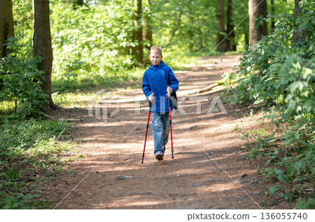 Teenager doing Nordic walking with poles in a sunny forest, enjoying nature, fresh air, and active outdoor recreation Teenager doing Nordic walking with poles in a sunny forest, enjoying nature, fresh air, and active outdoor recreation 136055740
