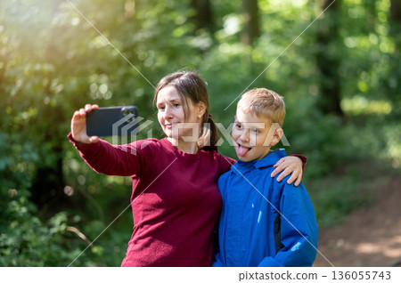 Happy mother and son taking a selfie together in a spring park, enjoying cheerful family moments outdoors 136055743