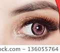 striking close up of a woman eyes accentuated by pink contact lenses, bold lashes, and shimmering makeup. Red framing the gaze, conveying fashion, confidence, and contemporary beauty 136055764