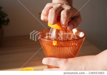 Squeezing orange juice using a manual juicer in the kitchen 136055863