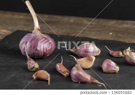 ripe garlic scattered on a black table in the kitchen and cloves of crushed garlic , garlic spices lie on a black slate board in the kitchen over cooking ripe garlic scattered on a black table in the kitchen and cloves of crushed garlic , garlic spices lie on a black slate board in the kitchen over cooking 136055882