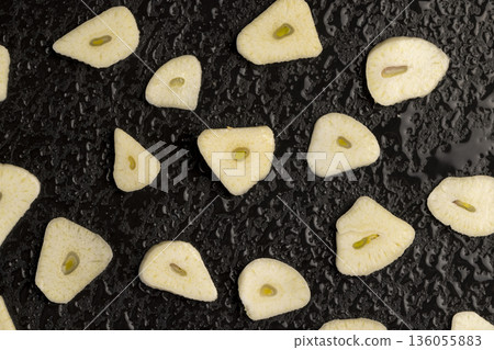 freshly peeled and sliced cloves scattered on black slate, peeled and sliced fragrant natural and fresh spices from garlic cloves scattered on black slate stone, covered with drops of water 136055883