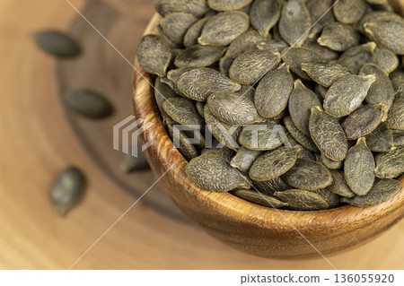 a large number of peeled large dried pumpkin seeds are lying on a wooden walnut board and in wooden dishes, a large number of healthy large pumpkin seeds without shells 136055920