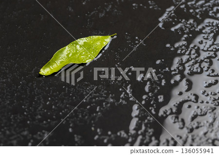wet black uneven and black slate for serving and green mandarin leaf covered with lots of water drops mandarin leaf and kitchen board made of black embossed slate 136055941