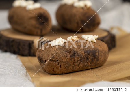a potato cake lies on a serving board and paper, a sweet classic cake made from butter and a large amount of cocoa mixed with sponge cake and cognac 136055942