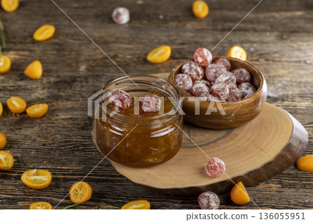 whole kumquat fruits in white powder, a glass jar with sweet orange jam on the table 136055951