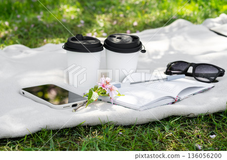 two paper cups of coffee or tea and a sakura branch on a light blanket, a notebook, a pen, glasses and a phone, freelancing in nature, coffee break two paper cups of coffee or tea and a sakura branch on a light blanket, a notebook, a pen, glasses and a phone, freelancing in nature, coffee break 136056200