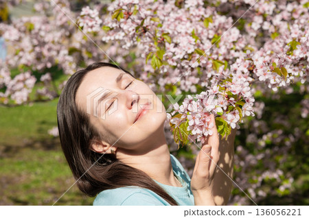Young woman with closed eyes enjoying scent of cherry blossoms in peaceful spring park 136056221