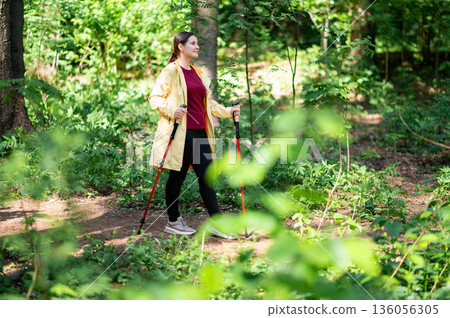Woman practicing Nordic walking with special poles on a sunny forest path, enjoying active lifestyle and fresh air Woman practicing Nordic walking with special poles on a sunny forest path, enjoying active lifestyle and fresh air 136056305