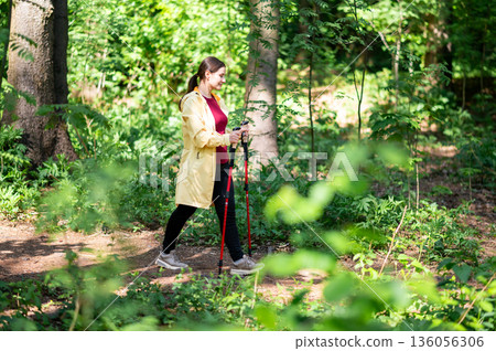 Woman doing Nordic walking alone in green forest, wearing sporty outfit, enjoying nature, movement, and mental balance Woman doing Nordic walking alone in green forest, wearing sporty outfit, enjoying nature, movement, and mental balance 136056306