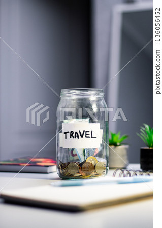 Travel savings in jar. Money being added to travel themed savings container. Inspires adventure planning and purposeful financial habits 136056452