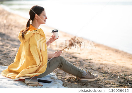 A young woman drinking coffee on the lake shore A young woman drinking coffee on the lake shore 136056615