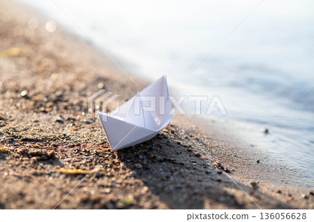 Paper boat on the lake shore, resting on wet sand near calm wate Paper boat on the lake shore, resting on wet sand near calm wate 136056628
