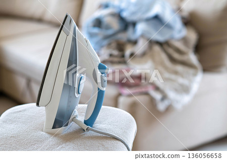 An iron on an ironing board with wrinkled linen in the background 136056658