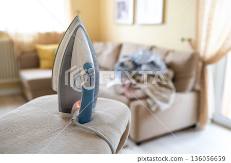 An iron on an ironing board with wrinkled linen in the background An iron on an ironing board with wrinkled linen in the background 136056659