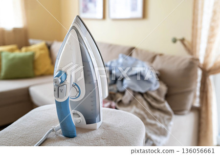 An iron on an ironing board with wrinkled linen in the background An iron on an ironing board with wrinkled linen in the background 136056661