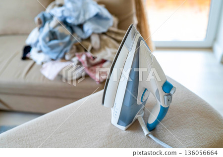 An iron on an ironing board with wrinkled linen in the background An iron on an ironing board with wrinkled linen in the background 136056664