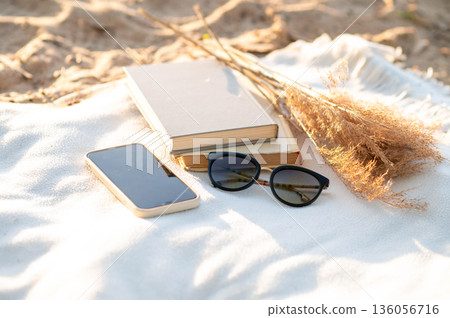 Minimal beach arrangement with tech and nature elements on a white blanket under warm sunshine Minimal beach arrangement with tech and nature elements on a white blanket under warm sunshine 136056716