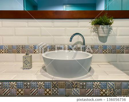 Modern bathroom sink with patterned tiles, mirror, and soap dispenser in a stylish interior setting Modern bathroom sink with patterned tiles, mirror, and soap dispenser in a stylish interior setting 136056736