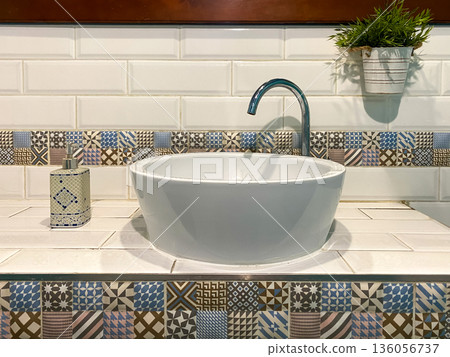 Modern bathroom sink with patterned tiles, mirror, and soap dispenser in a stylish interior setting Modern bathroom sink with patterned tiles, mirror, and soap dispenser in a stylish interior setting 136056737