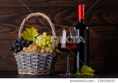 Red wine bottle with a glass and basket of fresh grapes 136056935