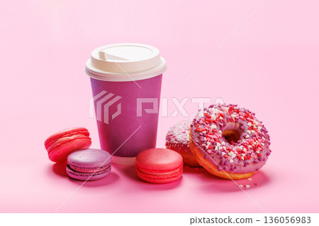 A cheerful display of colorful macarons, donuts, and a paper coffee cup on a pastel pink background A cheerful display of colorful macarons, donuts, and a paper coffee cup on a pastel pink background 136056983