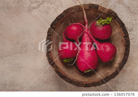 Fresh radishes in a rustic wooden bowl on a textured surface showcasing vibrant colors and natural textures 136057076