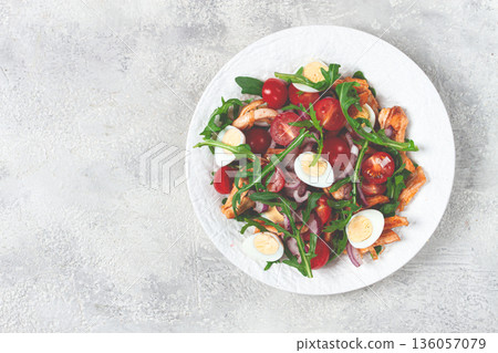 a warm salad with fried chicken fillet, arugula and cherry tomatoes, and boiled quail eggs, on a white plate, no people. a warm salad with fried chicken fillet, arugula and cherry tomatoes, and boiled quail eggs, on a white plate, no people. 136057079