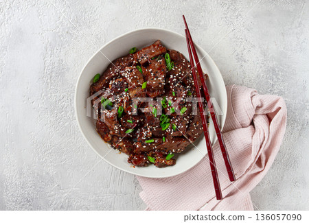 Crispy beef, with green onions and sesame seeds, in a bowl with chopsticks, on a textured surface, on a light background, no people Crispy beef, with green onions and sesame seeds, in a bowl with chopsticks, on a textured surface, on a light background, no people 136057090