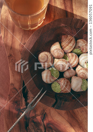 Snails cooked with herb oil on a wooden plate, served with white wine, natural light, no people, 136057091