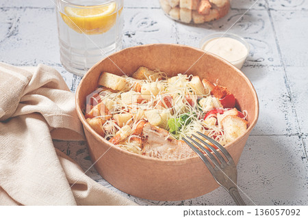 Caesar salad in a paper container, take it on the way, with sauce and croutons, on the table, snack, no people, 136057092