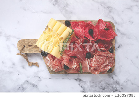 Assorted meat, appetizer, prosciutto, salami and ham, with maasdam cheese and olives, on a wooden board, breakfast, top view, close-up, no people Assorted meat, appetizer, prosciutto, salami and ham, with maasdam cheese and olives, on a wooden board, breakfast, top view, close-up, no people 136057095