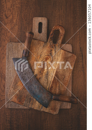 Old wooden cutting boards and a large curved knife on a rustic wooden table 136057104