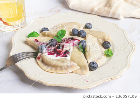 Delicious homemade dumplings served with berry sauce and fresh blueberries on a white plate Delicious homemade dumplings served with berry sauce and fresh blueberries on a white plate 136057109