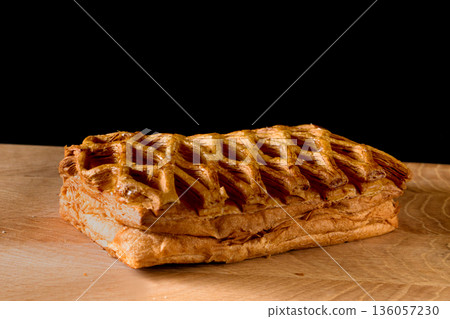 Confectionery, mesh-shaped puff pastry bun on wood board on black background Confectionery, mesh-shaped puff pastry bun on wood board on black background 136057230