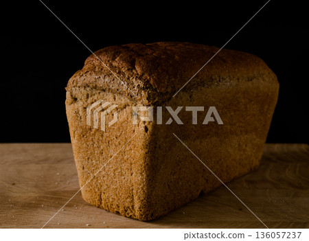 Loaf of black rye bread, in the shape of a brick on a wooden board on a black background Loaf of black rye bread, in the shape of a brick on a wooden board on a black background 136057237
