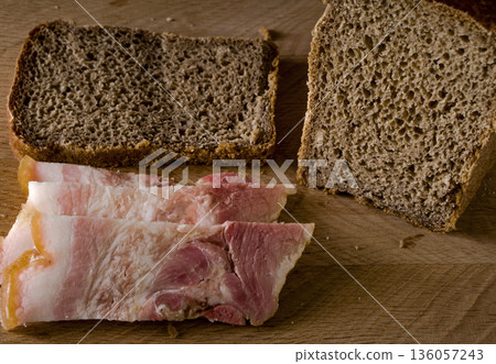 Black bread and salted lard with strips of meat on a wooden board 136057243