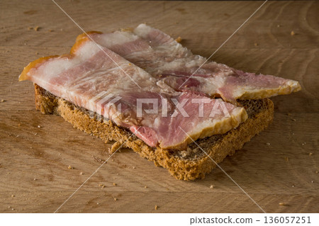 Sandwich of black bread and salted lard with strips of meat on a wooden board 136057251