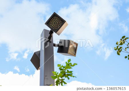 Modern outdoor lighting complex with multiple LED luminaires on single pole for urban illumination. Three consoles on single support, facing in different directions and at different angles Modern outdoor lighting complex with multiple LED luminaires on single pole for urban illumination. Three consoles on single support, facing in different directions and at different angles 136057615