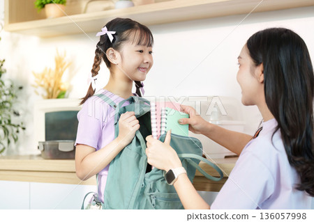 Back to School. A young girl joyfully receiving school supplies from her mother. 136057998