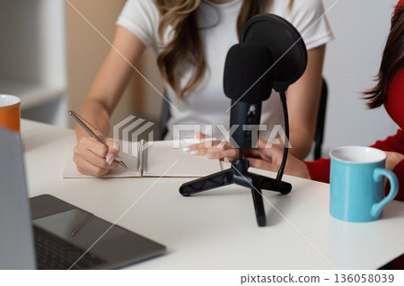 A woman is writing in a notebook while another woman sits behind her A woman is writing in a notebook while another woman sits behind her 136058039