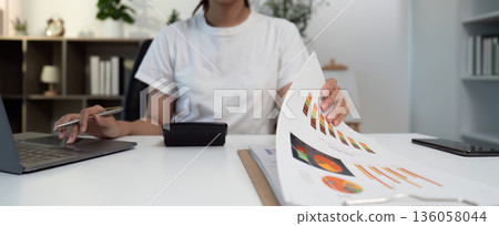 Business Analysis. Young woman reviewing financial documents and using a calculator. Business Analysis. Young woman reviewing financial documents and using a calculator. 136058044