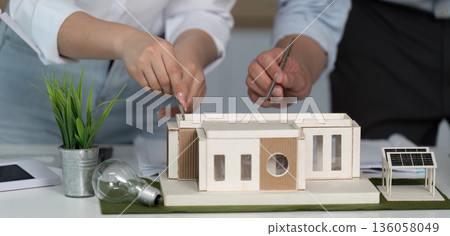 Two people are working on a model of a house Two people are working on a model of a house 136058049