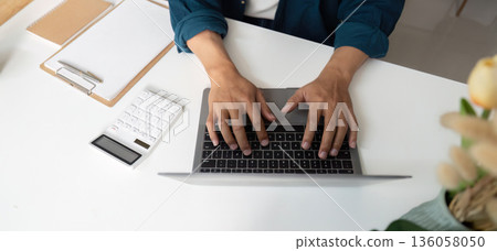 A man is typing on a laptop computer with a calculator A man is typing on a laptop computer with a calculator 136058050