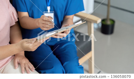 A woman in a blue uniform is sitting in a chair with a clipboard in front of her 136058070