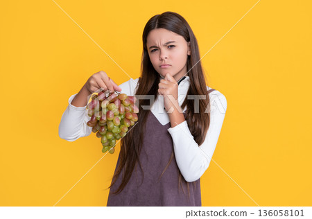 pondering child hold fresh grapes fruit on yellow background 136058101